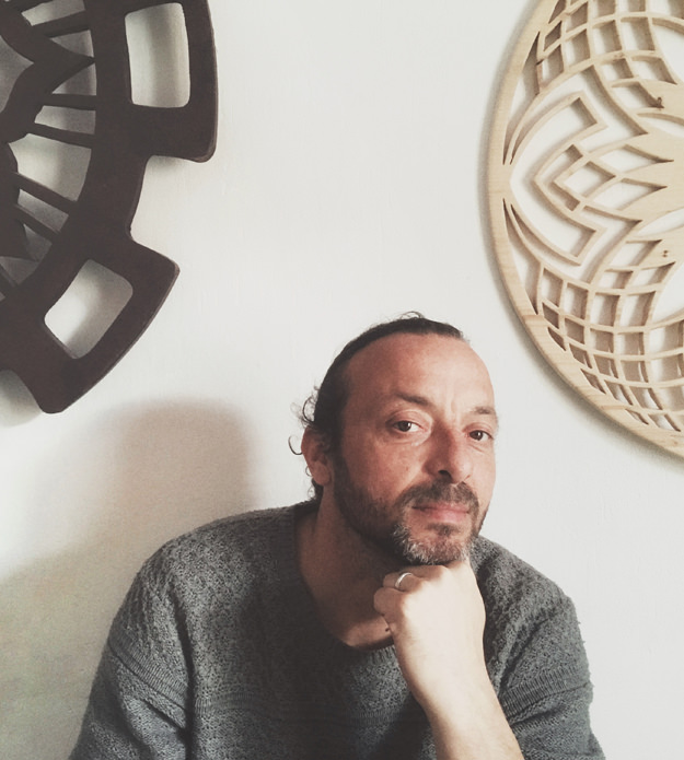 Portrait of woodcrafter Alexandre Daufin with two handmade wooden art mandalas on the wall